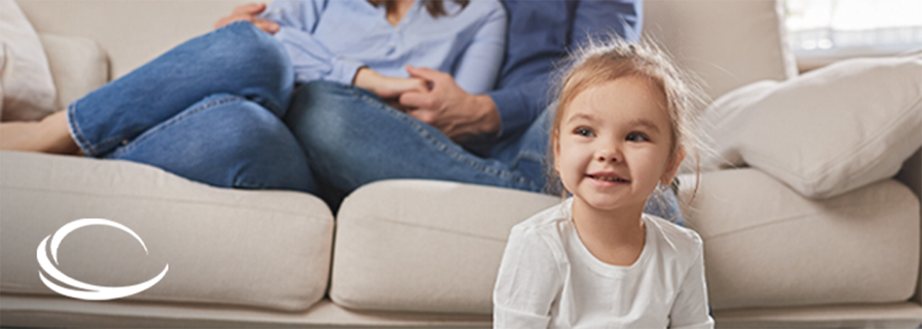 Girl sitting on the floor with her parents seated together on the couch above her