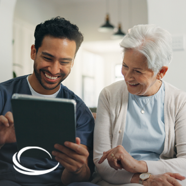 Healthcare professional sitting next to older woman on sofa and showing her some information on a tablet